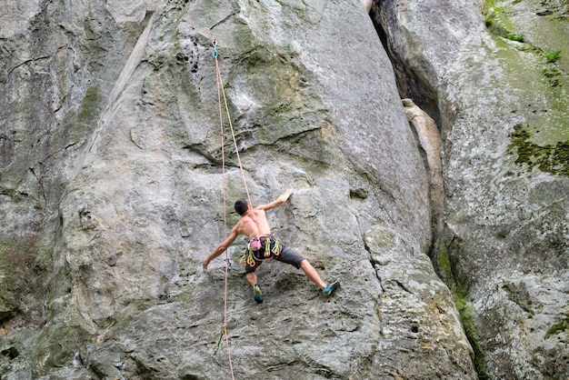 Strong male climber climbing steep wall of rocky mountain. Sportsman overcoming difficult route. Engaging in extreme sports hobby concept.