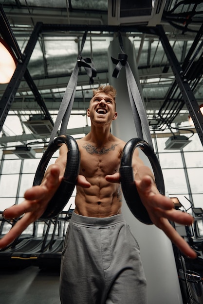 Strong man doing exercise on to gymnastic rings at gym Fit male athlete training on gymnastic rings in light sport hall