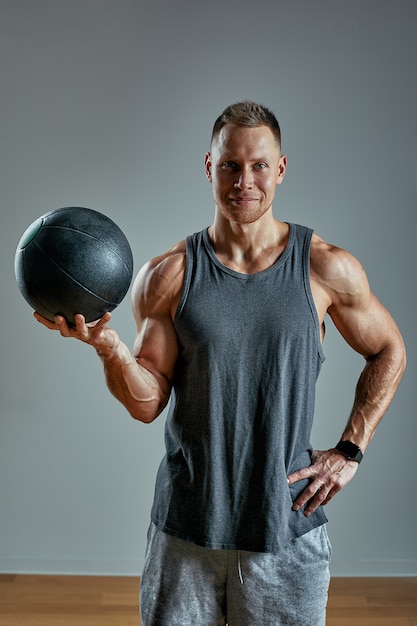 Strong man doing exercise with med ball. Photo of man perfect physique on grey background. Strength and motivation.