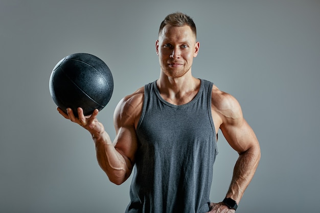 Strong man doing exercise with med ball. Photo of man perfect physique on grey wall. Strength and motivation.