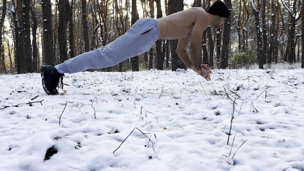 Strong man doing push ups on snow at winter forest Sportsman exercising at nature Young guy training outdoor Muscular athlete showing hard and intense workout Concept of sportive lifestyle