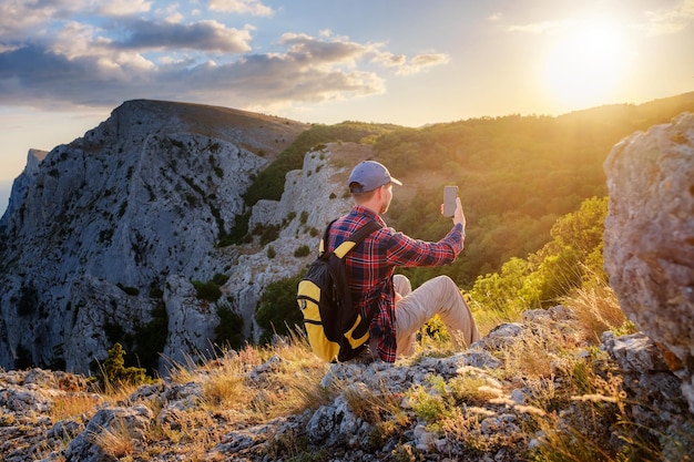 Strong man hiker taking photo with smart phone at mountain peak