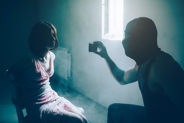 Photo strong and muscular man in black mask is holding phone in front of girl and looking at her.