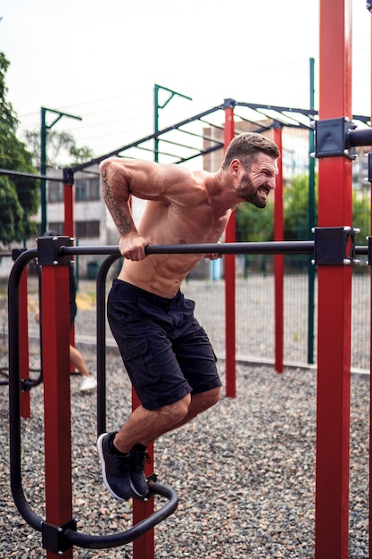 Strong muscular man doing push-ups on uneven bars in outdoor street gym