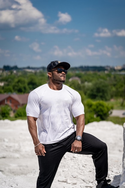 Strong muscular man in whitr shirt on beautiful landscapes. Athlete on sunny day standing in nature.