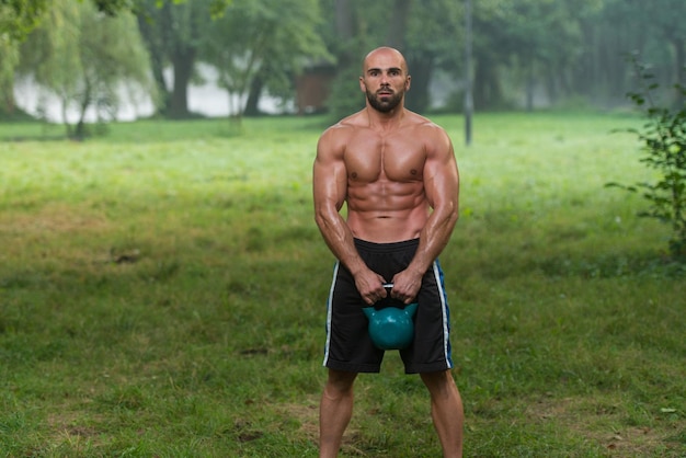 Strong And Muscular Young Fitness Man Holds Up A Green Kettlebell Outdoors Sports And Fitness Concept Of Healthy Lifestyle Fitness Male