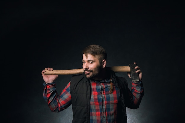 Strong smirking seductive worker holding axe. Adult woodsman on dark background, confident lumberjack portrait closeup. Sexy rural male, strength concept