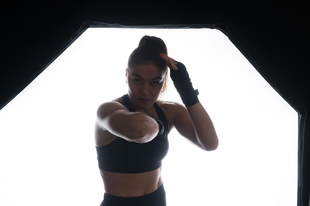 Strong sportswoman in boxing gloves prepared high kick isolated on white red yellow background