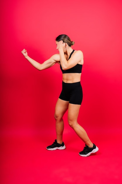 Strong sportswoman in boxing gloves prepared high kick isolated on white red yellow background