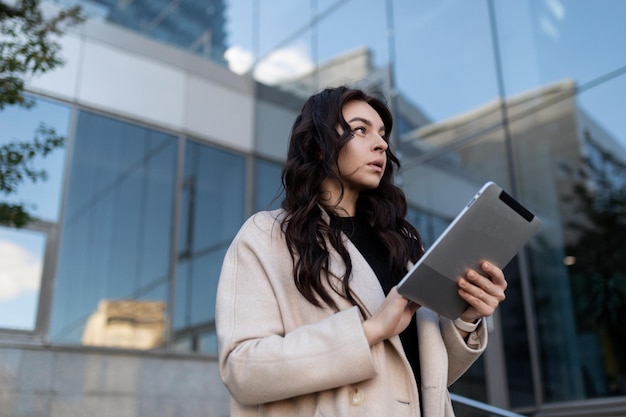 Strong successful businesswoman with a tablet in her hands on the background of an office building