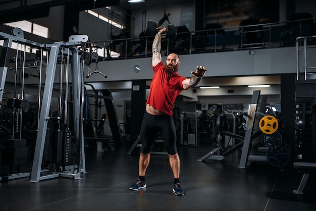 Strong weightlifter doing exercise with dumbbells, workout in gym.