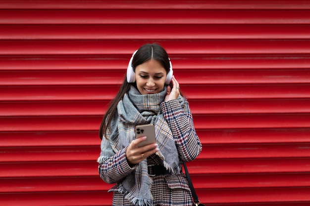 Strong woman on the background of a red wall in headphones chooses a track on a mobile phone