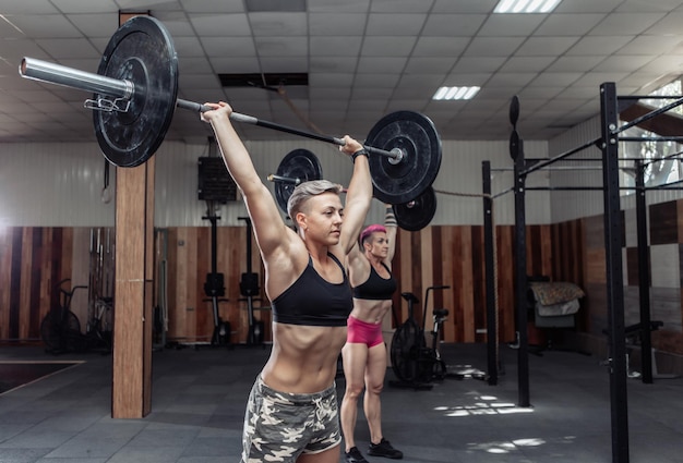 Strong women bodybuilder doing overhead with heavy barbell in modern cross gym. Functional training class. Bodybuilding and Fitness