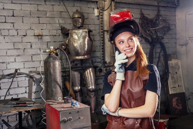 Strong and worthy pretty redhead ginher woman wearing protection helmet and leather apron with gloves holding welding machine instrument small business concept