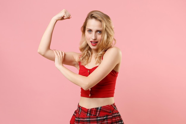 Photo strong young blonde woman girl in red sexy clothes posing isolated on pastel pink background studio portrait. people sincere emotions lifestyle concept. mock up copy space. showing biceps, muscles.