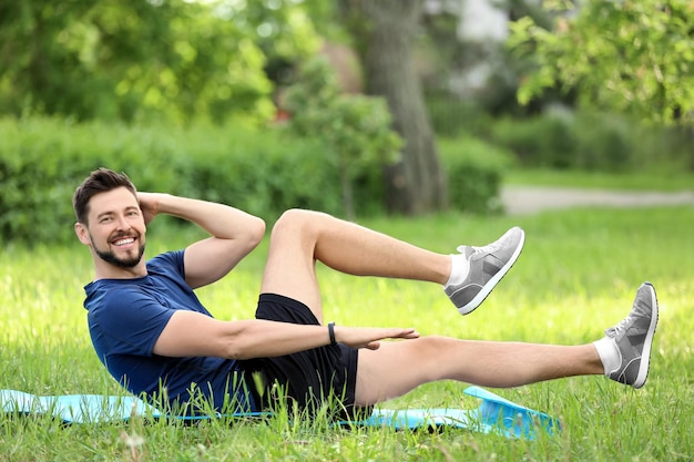 Strong young man doing bicycle crunch exercise on green meadow