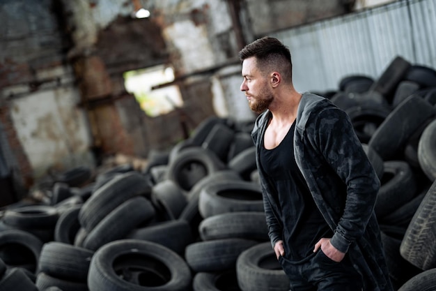 Strong young man posing at the abandoned place with tires at the background Big muscles and perfect abs Many tires on the background Strongman after workout