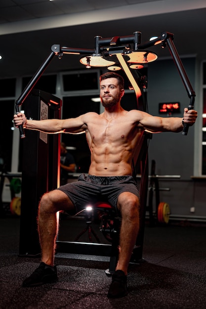 Strong young shirtless man working out in the gym Muscular athletic training man