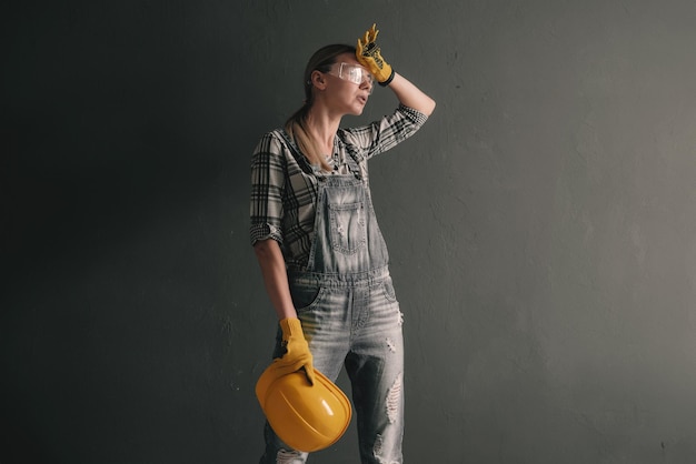 A strongwilled woman in a construction helmet mittens goggles and overalls is engaged in repair and construction work at home concept of a strong and independent woman