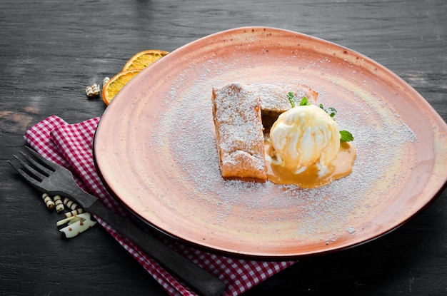 Strudel with apples and ice cream on a plate Dessert On a wooden background Free copy space Top view