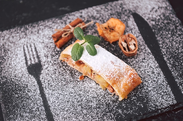 Strudel with apples, raisins and walnuts in rustic style on a dark background