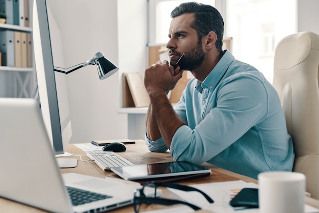 Stuck in office. Young modern businessman looking away while sitting in the office