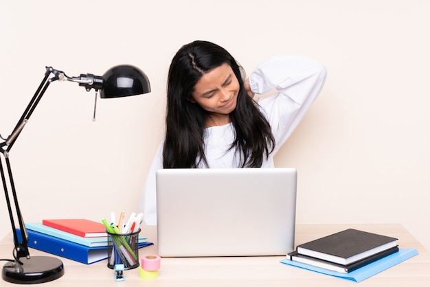 Student asian girl in a workplace with a laptop on beige wall with neckache