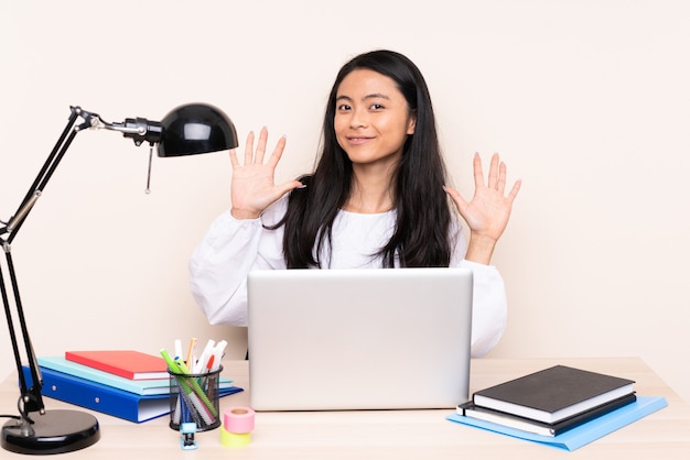 Student asian girl in a workplace with a laptop isolated on beige counting ten with fingers