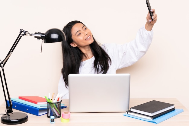 Student asian girl in a workplace with a laptop isolated on beige making a selfie