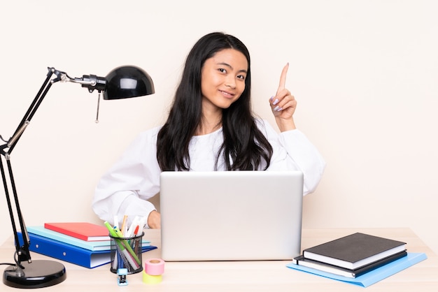 Student asian girl in a workplace with a laptop isolated on beige showing and lifting a finger in sign of the best