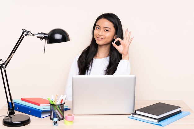 Student asian girl in a workplace with a laptop isolated on beige