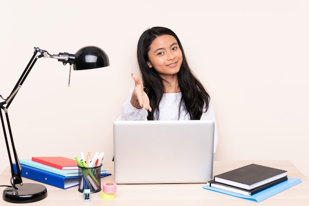 Student asian girl in a workplace with a laptop isolated on beige