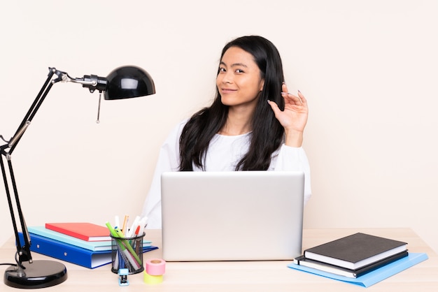 Student asian girl in a workplace with a laptop isolated on beige