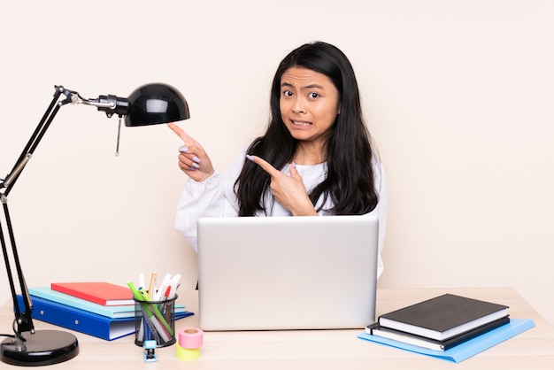 Student asian girl in a workplace with a laptop isolated on beige