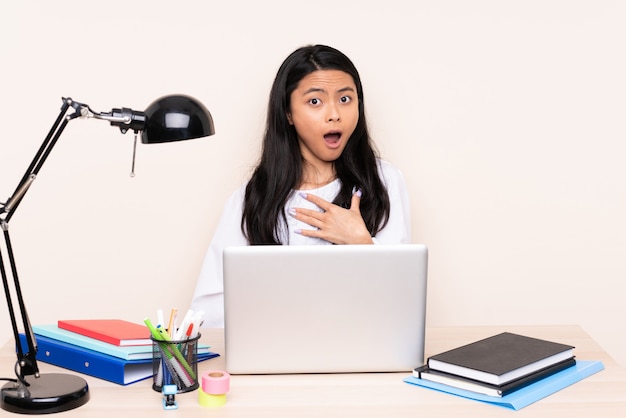 Student asian girl in a workplace with a laptop isolated on beige