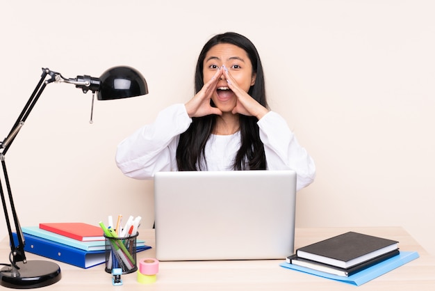 Student asian girl in a workplace with a laptop isolated on beige