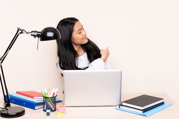 Student asian girl in a workplace with a laptop isolated on beige