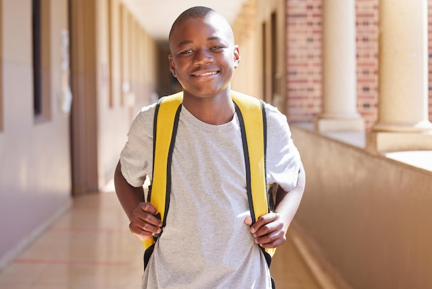 Student child and backpack standing in school campus lobby for study Back to school portrait African boy and ready for education learning or knowledge with happy smile in high school building