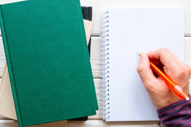 Student doing homework, writing in a notebook next to a stack of books