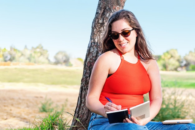 Student girl sitting outdoors in nature park writing notes in notebook