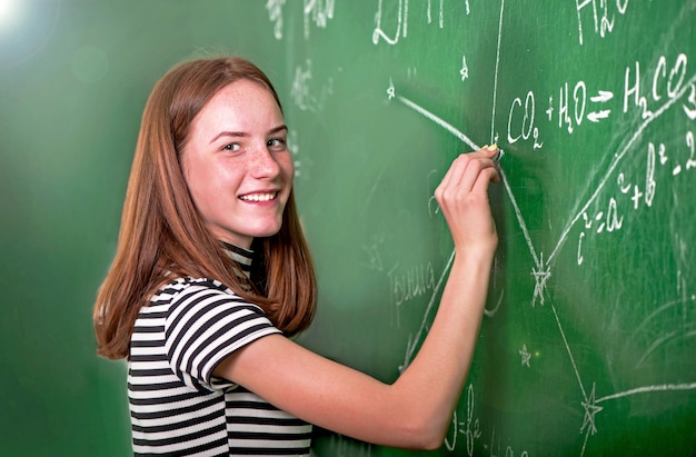 Student girl standing near clean blackboard in the classroom