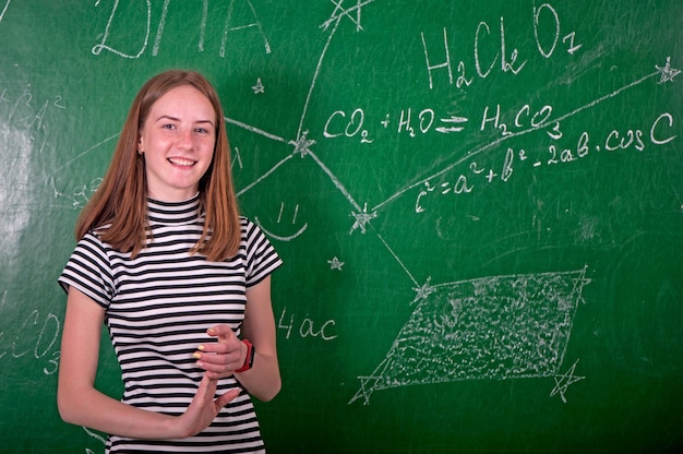 Student girl standing near clean blackboard in the classroom