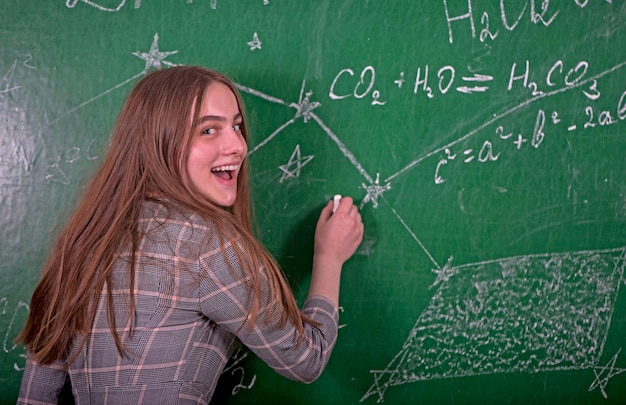 Student girl standing near clean blackboard in the classroom