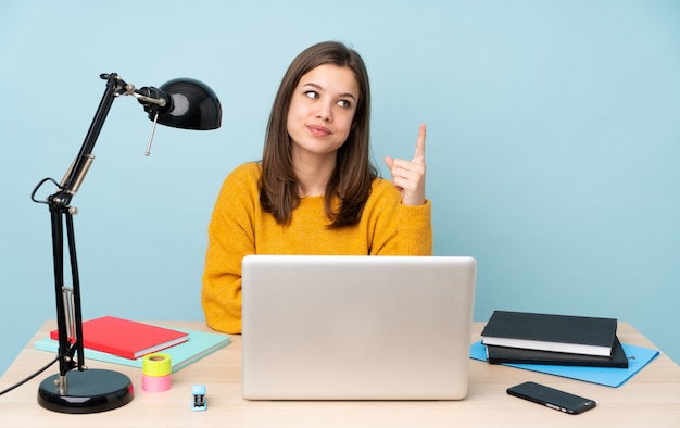 Student girl studying in her house on blue showing and lifting a finger in sign of the best