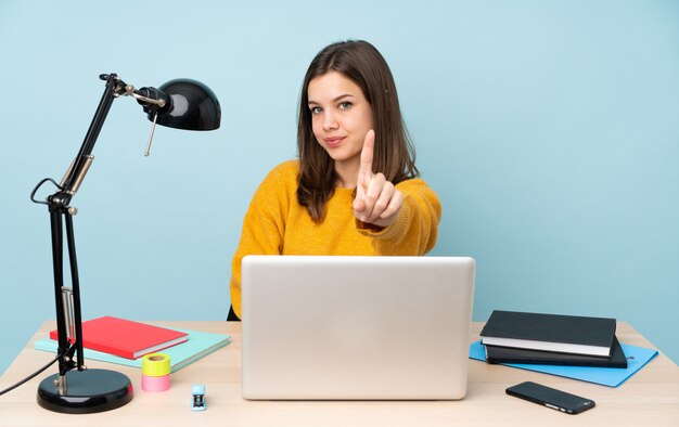 Student girl studying in her house isolated on blue wall showing and lifting a finger