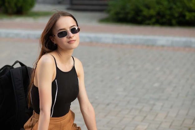 A student girl with a backpack is sitting on a bench in a city Park smiling