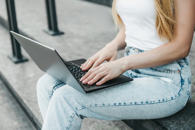 Student girl with laptop sitting on stairs against the background of the university building