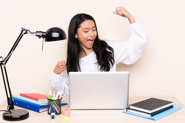 Student girl in a workplace with a laptop isolated on beige celebrating a victory