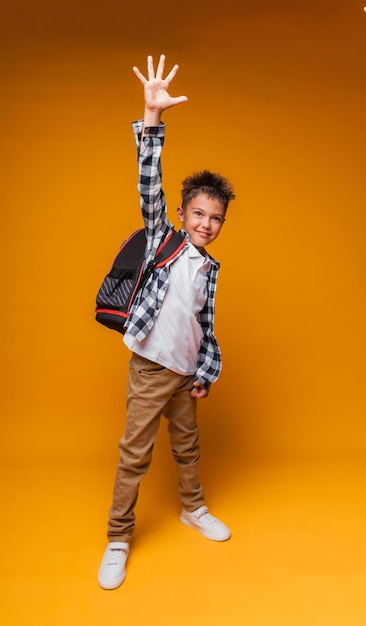 A student greets on a yellow background portrait of a boy with a backpack and a folder