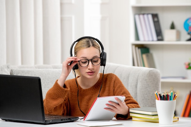 Student online cute girl in glasses and sweater studying on computer holding notepad